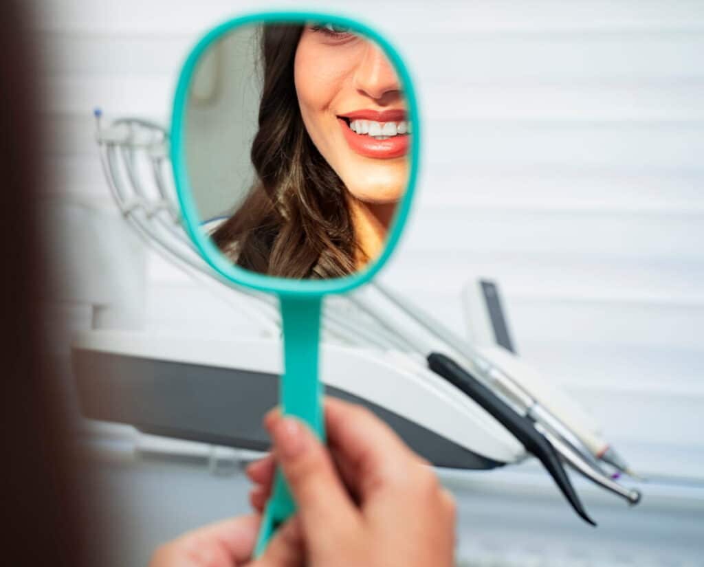 A woman smiling into the mirror after receiving an in-office teeth whitening treatment.