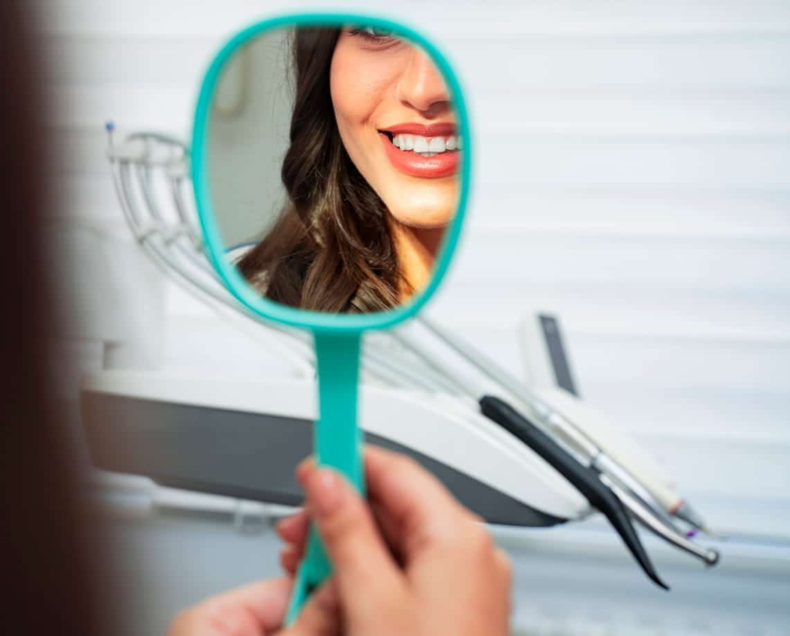 A woman smiling into the mirror after receiving an in office teeth whitening treatment