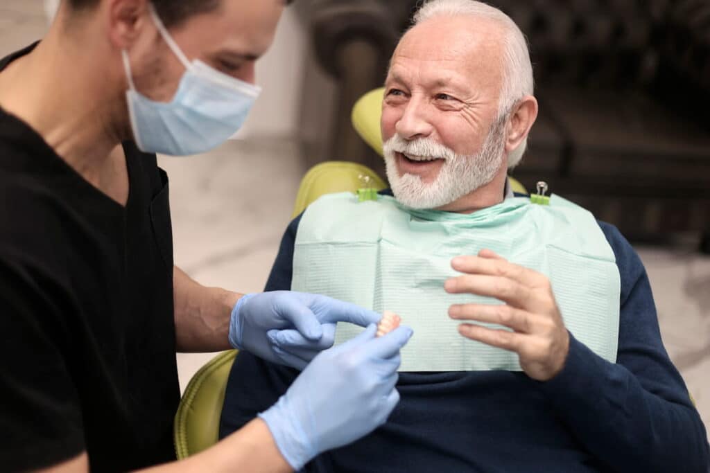 An older man smiling while taking to the dentist about limiting tooth loss.