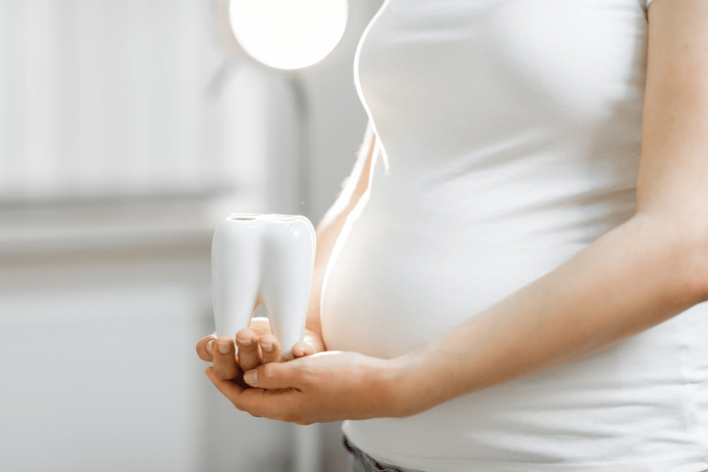 Focus is on a baby belly, as the mother holds a large model of a tooth in her hands.