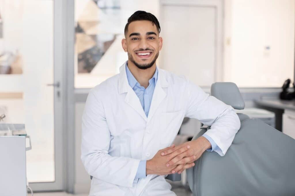 A Las Vegas dentist smiling while posing next to a dental office chair.