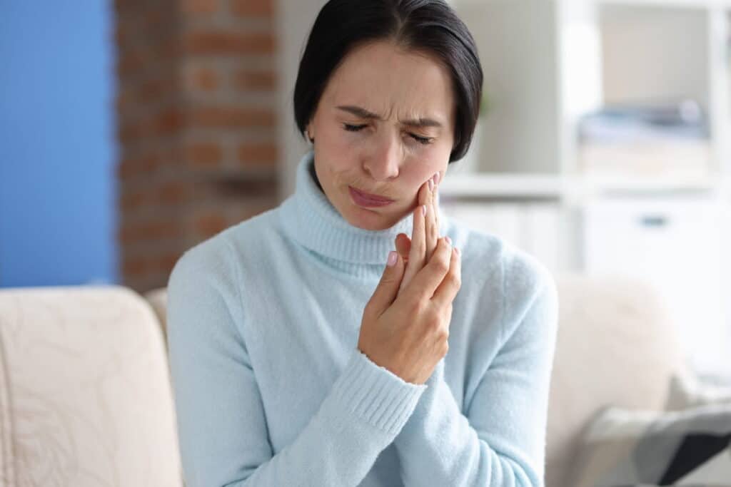 A woman experiencing a dental emergency as she holds her jaw in pain.