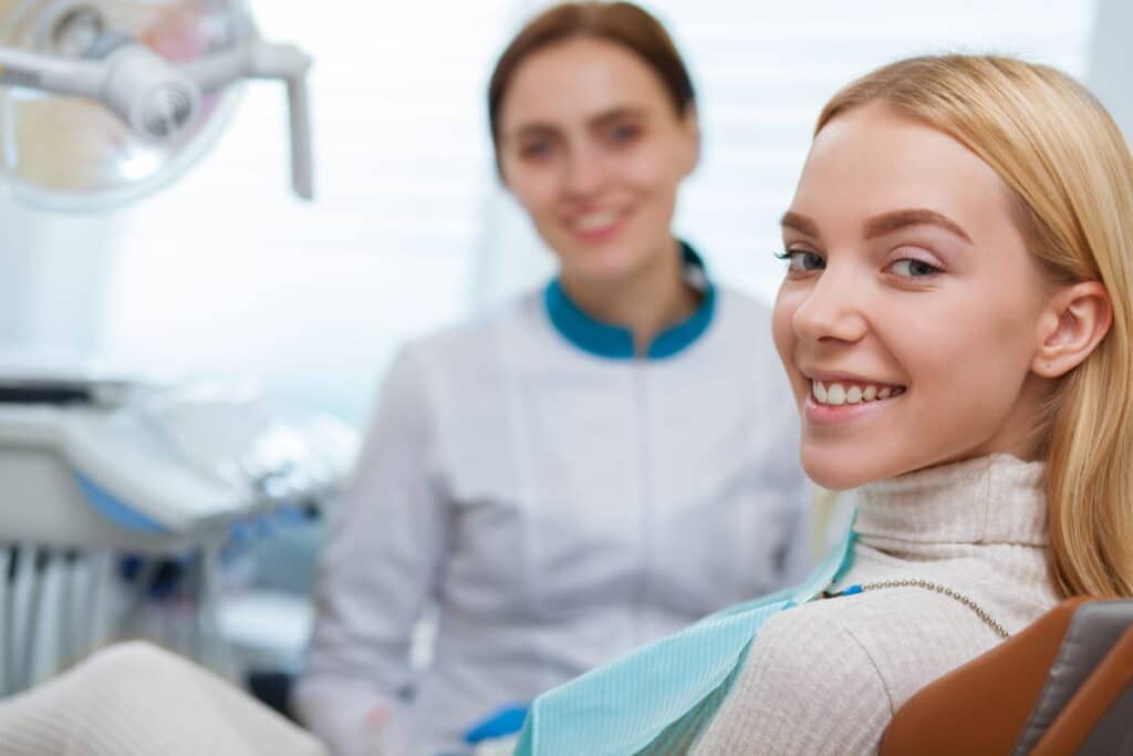 A woman in a dental chair smiling after being seen by a las vegas dentist for a dental emergency. The dentist is blurred out in the background.