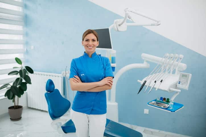 A female dentist smiling with her arms crossed as she stands in front of her dental chair in Minden, NV. 