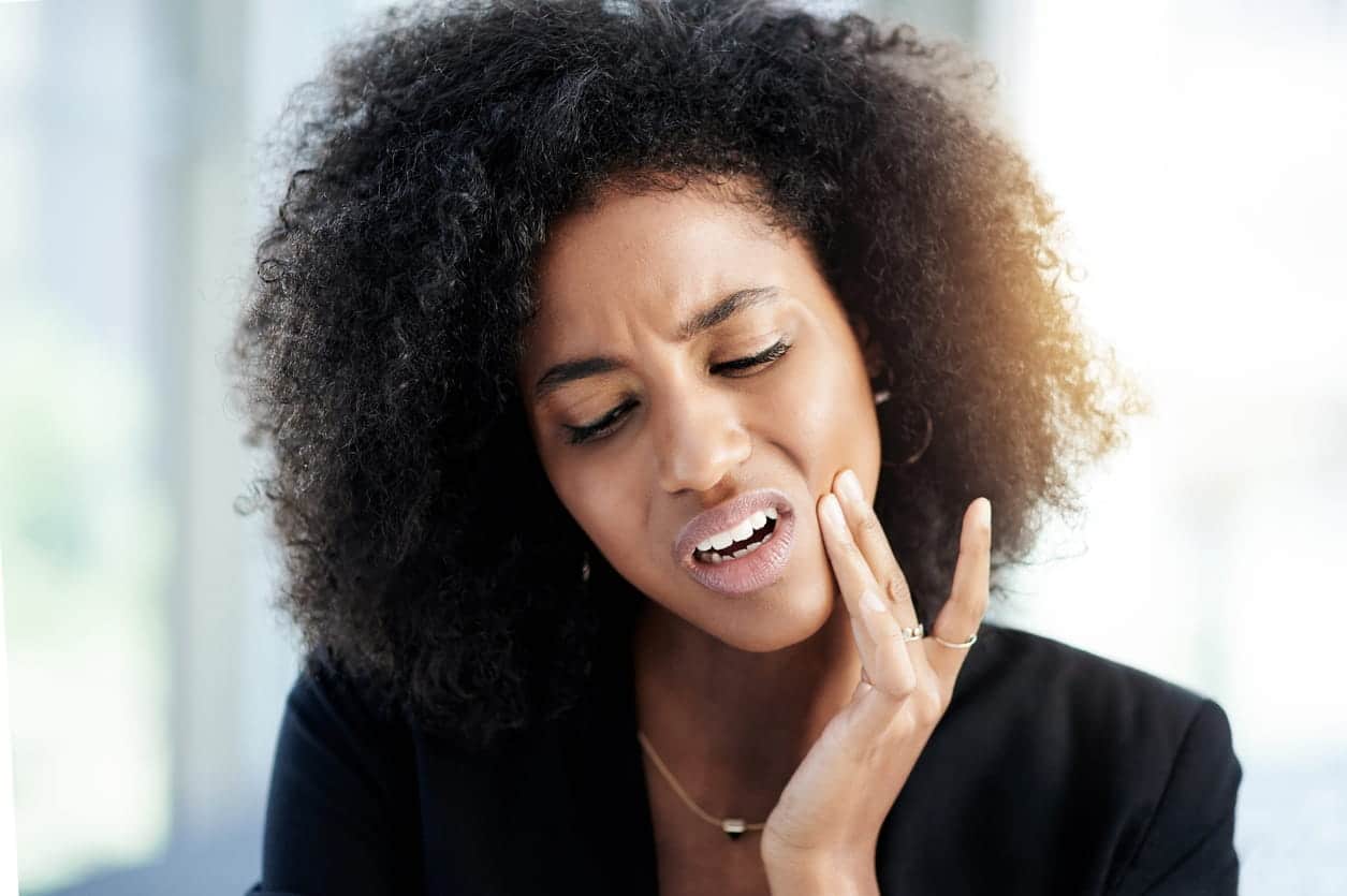 A woman is holding her jaw in pain after experiencing a dental emergency.