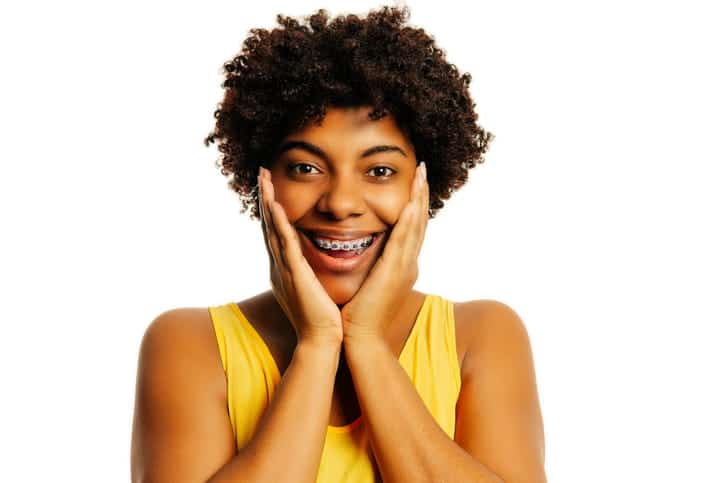 A woman holding her face while smiling with braces.