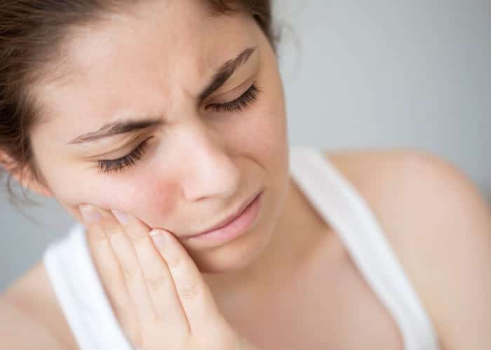 A woman is holding her face in pain while having a dental emergency. 