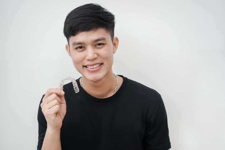 A teen holding his Invisalign retainer while smiling.