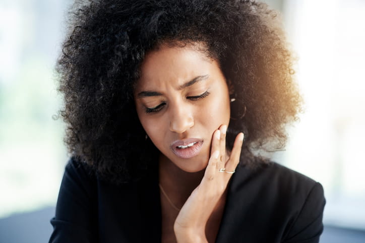 A woman holding her face in pain as she experiences a dental emergency.