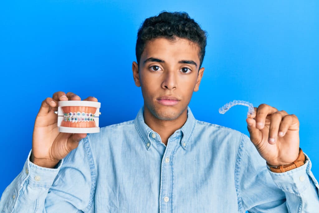 Sad teenager holding a model of teeth with braces and a retainer.