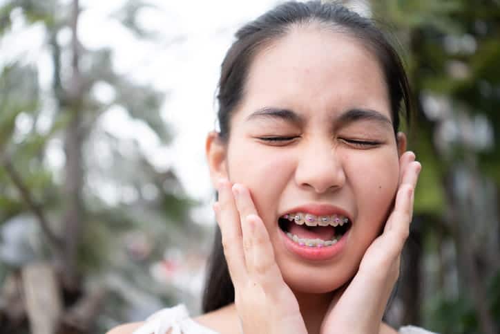 A teenager holds her face in pain due to wire irritations from her braces.