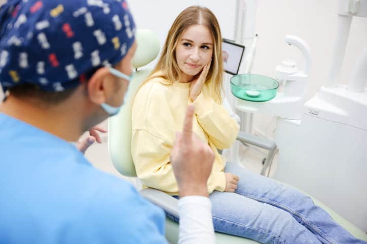 A dentist speaking to a woman who is holding her face in pain after breaking a tooth. 