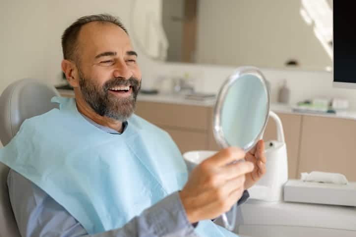 A man smiling into the mirror at a dentist's office after having his tooth fixed. 