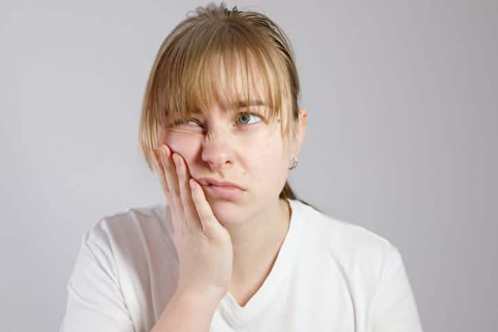 A woman holding her jaw in pain after experiencing wisdom tooth extraction complications. 