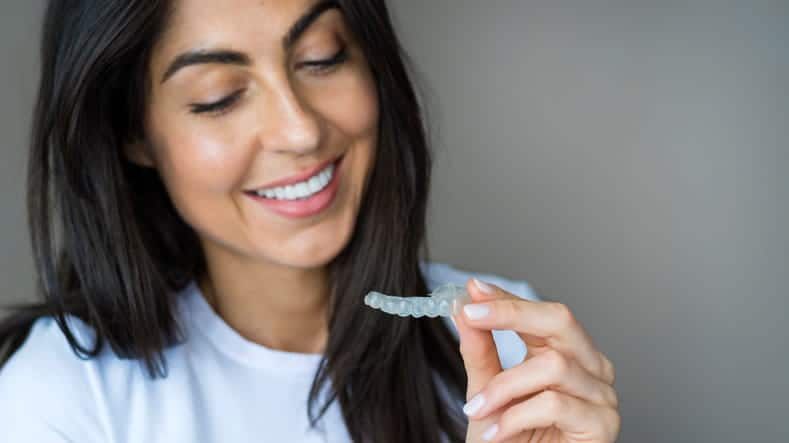 A woman smiles as she holds her clear retainer.