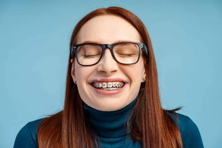 A woman with her eyes closed as she smiles with metal braces. 