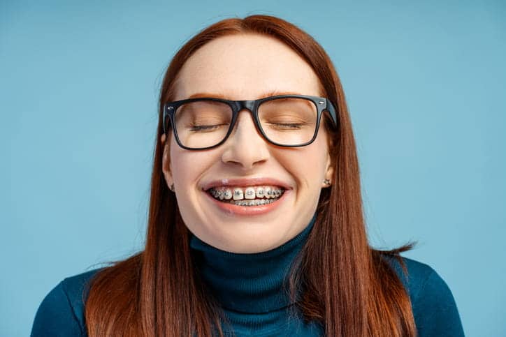 A woman with her eyes closed as she smiles with metal braces.