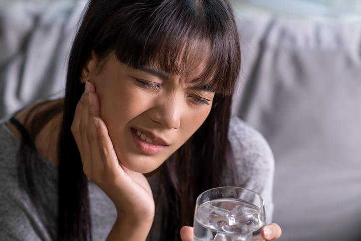 A woman holding her face in pain after experiencing a dry socket after wisdom tooth removal.