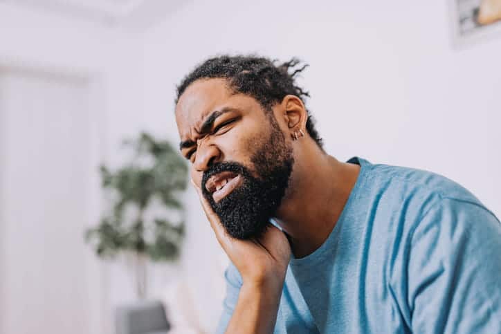 A man holding his jaw in pain after experiencing wisdom tooth extraction complications.