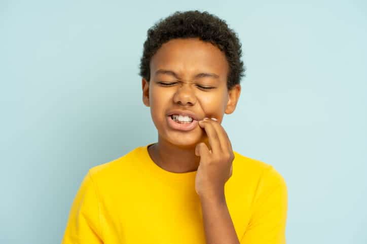 A young kid holding his face in pain after a dental emergency.