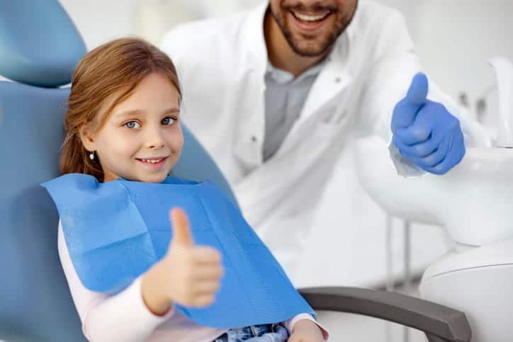 A young girl and a pediatric dentist giving a thumbs up before she gets a teeth cleaning.