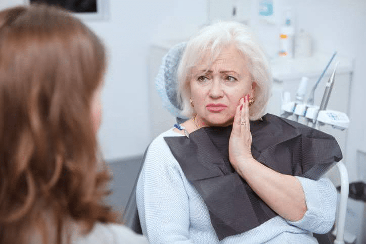An older woman holding her face in pain while seeing an emergency dentist.