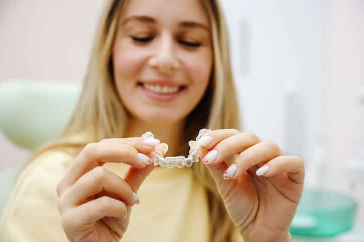 A woman smiles as she holds her Invisalign aligner.