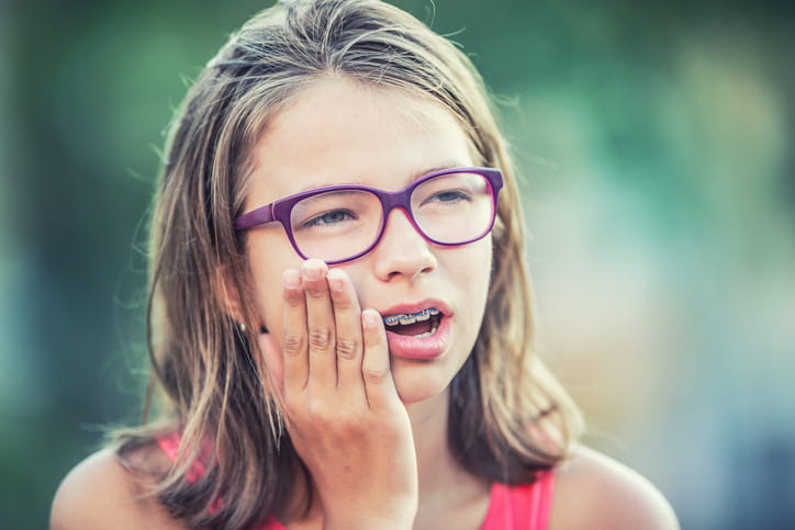 A girl holding her face in pain as she's having an orthodontic emergency.