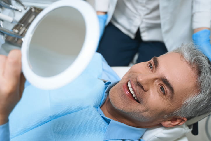 A man smiling into a mirror while he's in a dental chair.