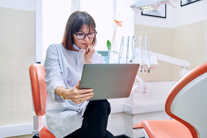 A dentist in a patient room while speaking to them on her tablet during a teledentistry appointment.