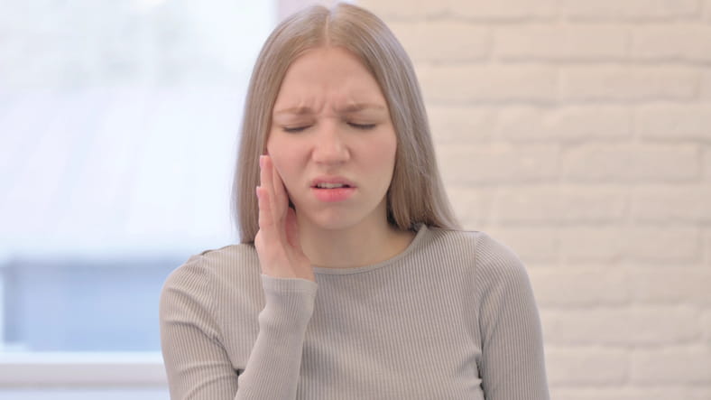 A woman holding her face in pain after losing a filling.