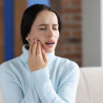 A woman holding her face in pain due to a dental emergency.