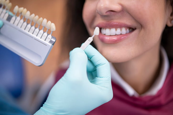 A dentist uses a palette tooth color sample to compare shades against a woman's smile. 