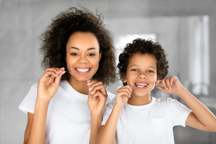 A mother and son smiling together while they floss their teeth.