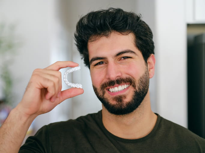 A man smiling as he holds his Invisalign aligner tray. 