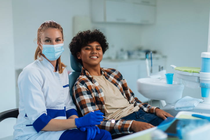 A patient smiling in a dental chair as him and the dentist pose for a photo. 