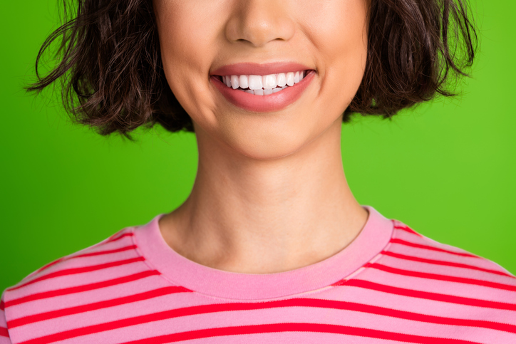 The focus is on a woman smiling. She's wearing a pink shirt and there is a bright green background. 