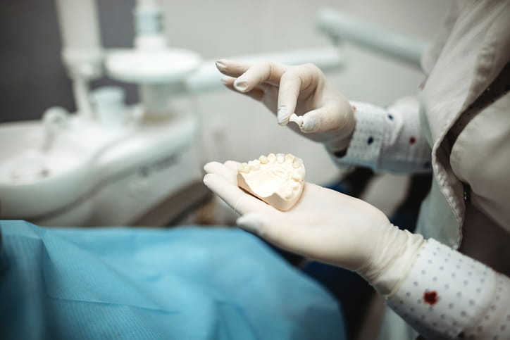 A dentist holds a dental crown as they test it with a mold of a patient's jaw. 