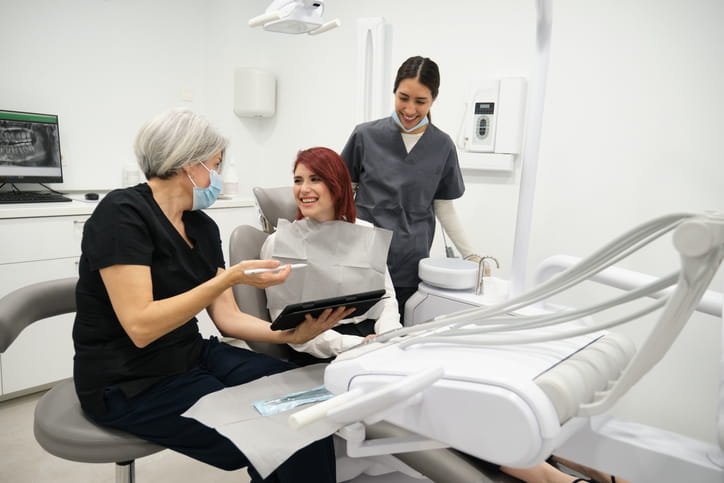 Two dentists talk and laugh with a patient at her first dental appointment.