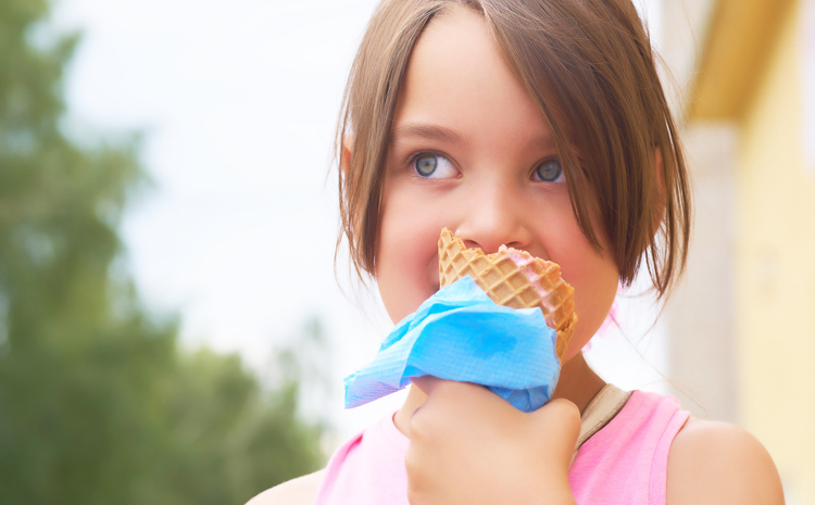 11 Common Foods That Cause Cavities In Kids 1 Pretty little girl eating licking big ice cream in waffles cone happy laughing on nature background