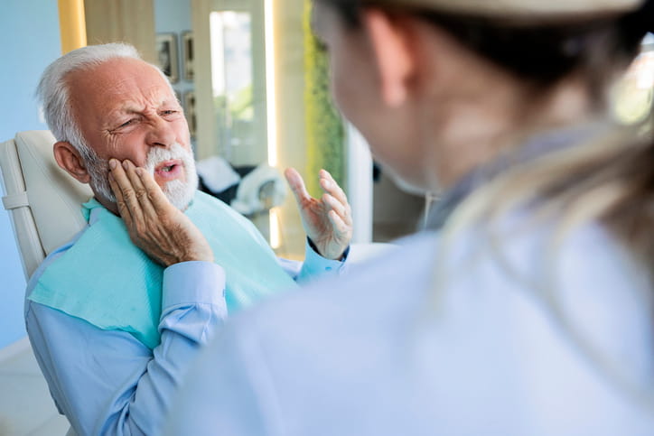 A man holds his face in pain due to a dental infection as he speaks to his dentist. 