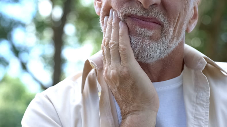 A man holding his face in pain due to a broken tooth. 