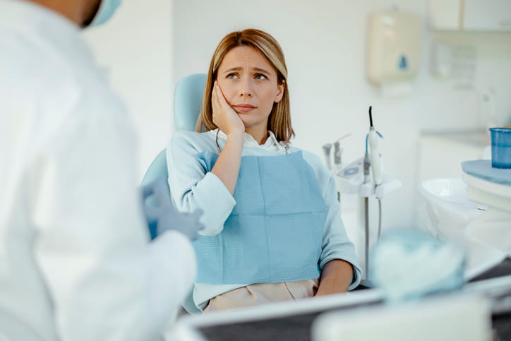 A woman with a tooth infection holding her face in pain while sitting in a dental chair. 