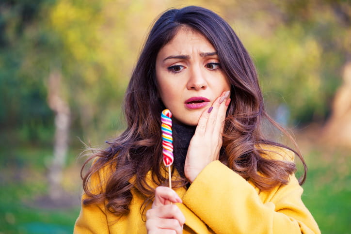 A woman holding her face in pain as she tries to eat candy.