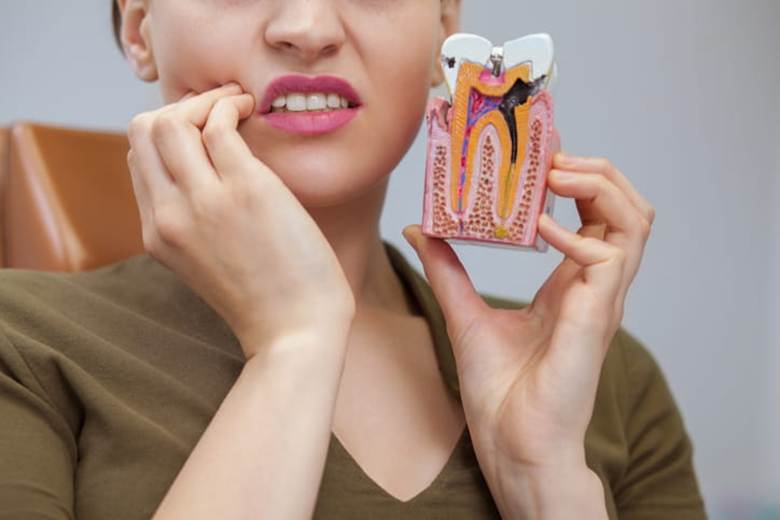 A woman holding her face in pain due to a dental emergency as she holds up a tooth model.