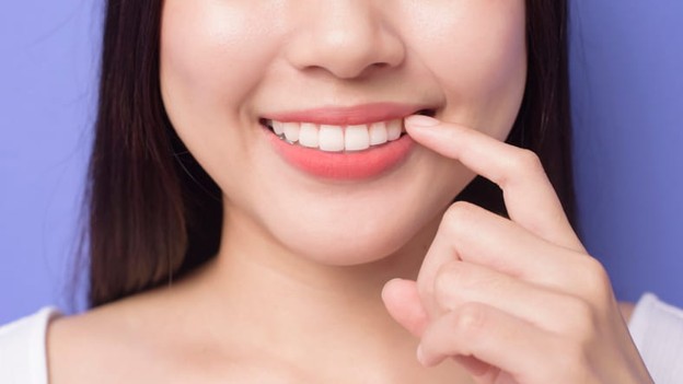 It’s Never Too Late To Visit The Dentist And Take Care Of Your Smile 1 A woman points at her mouth as she smiles.