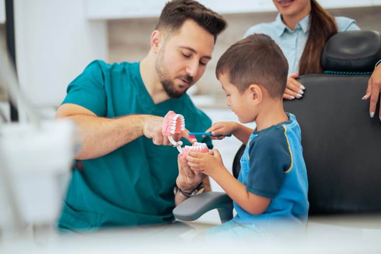 Absolute Dental Hosts Smiles For Nevada Kids Day 1 A dentist teaches a child about dental hygiene with a model of a mouth.